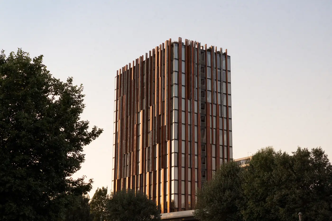 A slender tower clad in weathered-steel fins at dusk